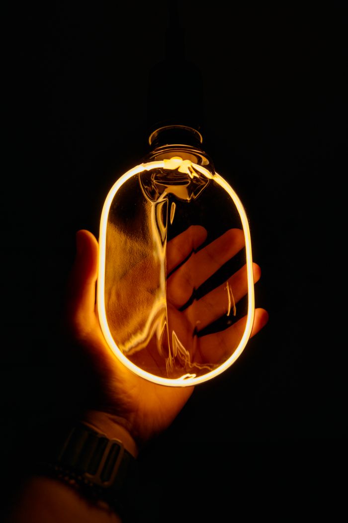 A hand holding a glowing filament bulb creates a cozy and warm ambiance against a dark background.